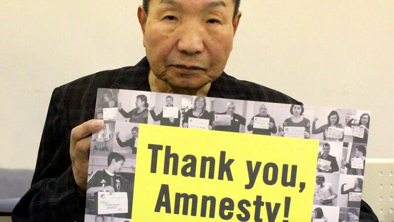 Iwao Hakamada hält ein Schild in die Kamera mit der Aufschrift "Thank you, Amnesty!"