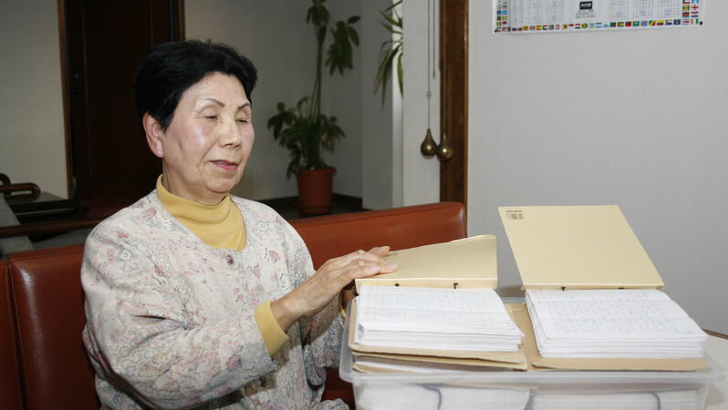 Eine Frau sitzt vor Ordnern und Boxen voller Briefe