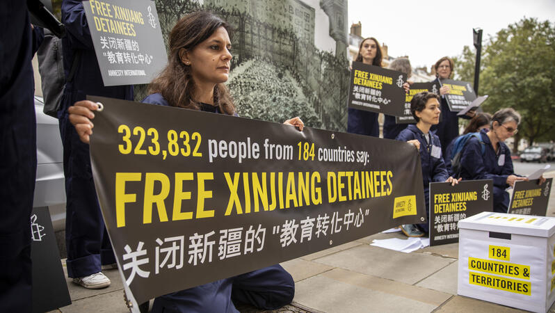 Das Bild zeigt mehrere Menschen, die mit Plakaten demonstrieren, darauf zu lessen "Free Xinjiang Detainees"