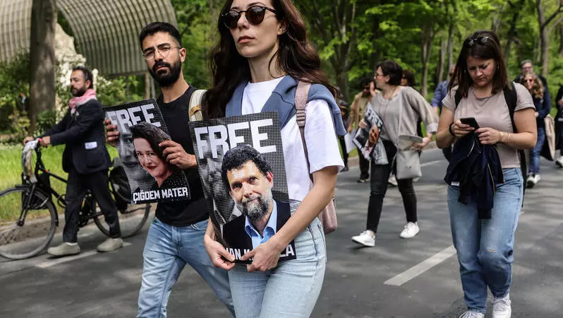 Das Foto zeigt mehrere Personen auf einer Straße in einem Protestzug. Sie halten Porträtfotos vor sich. Eines der Fotos zeigt Osman Kavala.