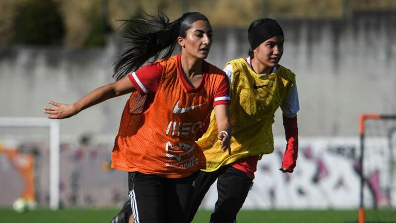 Das Foto zeigt zwei Fußballerinen auf einem Fußballplatz, die nebeneinander herlaufen.