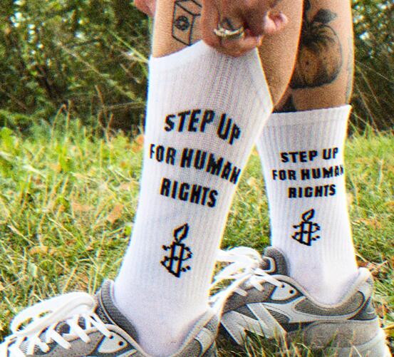 Man sieht eine Person, die weiße Socken und Sneaker trägt, auf den Socken steht "Step up for Human Rights"