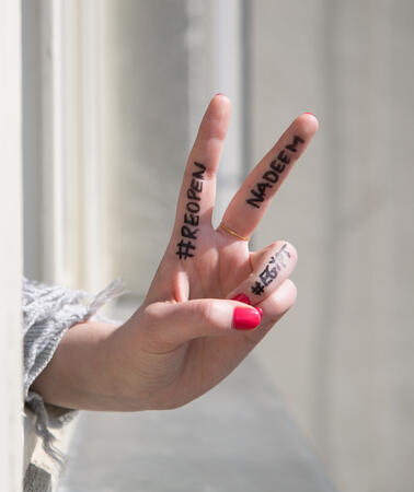 Eine Hand macht das Victory-Zeichen. Auf ihrem Zeigefinger, Mittelfinger und Ringfinger steht #ReopenNadeem und #Egypt