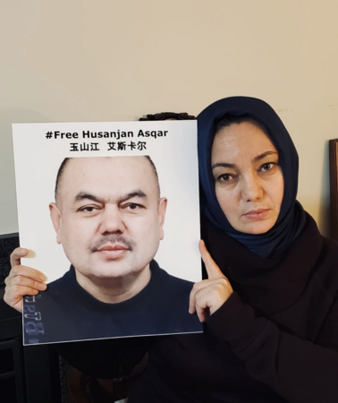 Eine Frau hält ein Plakat mit dem Foto eines Mannes, auf dem "#Free Husenjan Asqar" steht