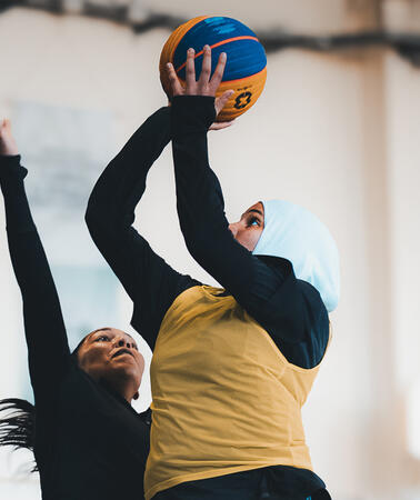 Das Bild zeigt zwei Basketballspielerinnen, eine versucht zu werfen, die andere blockt.