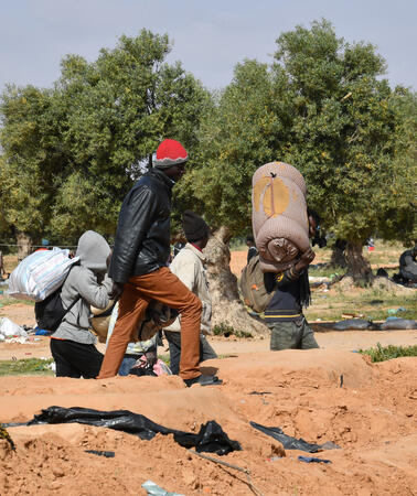 Mehrere Menschen mit Gepäck, Bündel stehen auf einem Feld, sie verlassen das Gelände