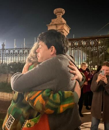Zwei Personen, Sean Binder und seine Mutter, umarmen sich. Menschen, die dabei stehen, machen Fotos