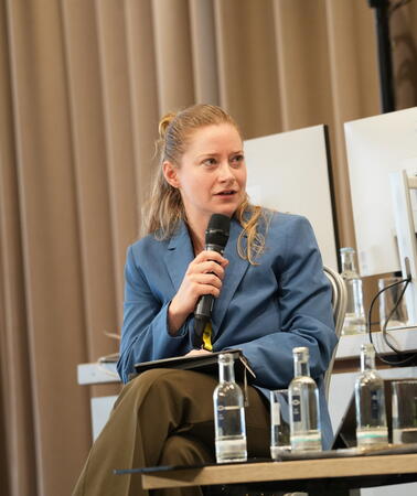 Porträt von Lisa Nöth, die auf einer Bühne in ein Mikrofon spricht