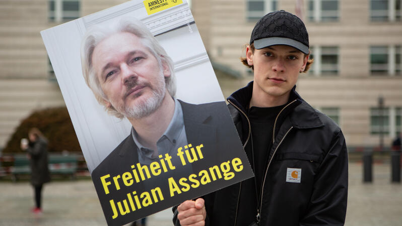 Das Bild zeigt einen jungen Mann mit einem Protestplakat "Freiheit für Julian Assange"