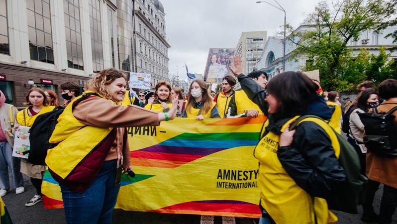 Das Foto zeigt mehrere Personen mit Amnesty-Leibchen an der Spitze eines Demonstrationszuges. Viele Lachen, andere tragen Mundschutz. Sie halten ein Banner vor sich mit Regenbogenfarben und dem Amnesty-Logo.